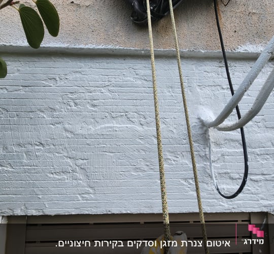 קיר צבוע בלבן עם חבלים תלויים ועבודות גובה